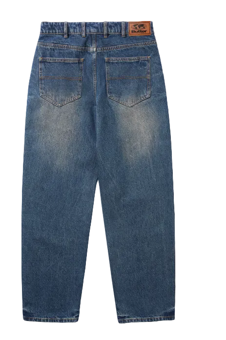 Back view of a pair of blue denim jeans with a faded wash, featuring a brown leather patch on the back waistband and two back pockets, displayed on a white background.